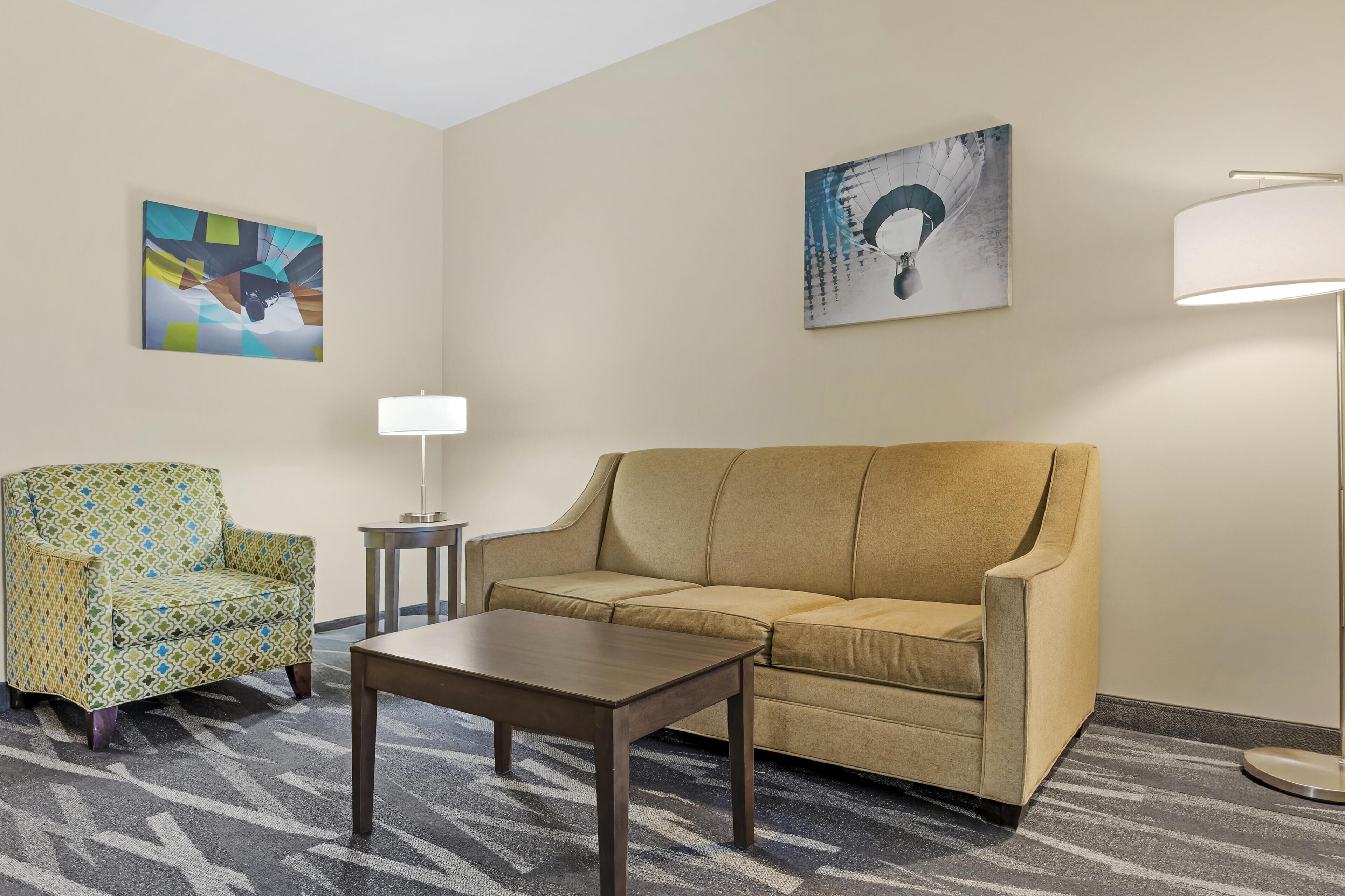 Une pièce avec un canapé beige, un fauteuil à motifs, une petite table et deux lampes fixées au mur.