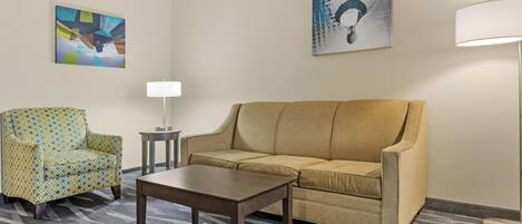 Une pièce avec un canapé beige, un fauteuil à motifs, une petite table et deux lampes fixées au mur.