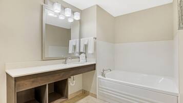 Un baño moderno con un espejo grande, un tocador con lavamanos y una bañera independiente.
