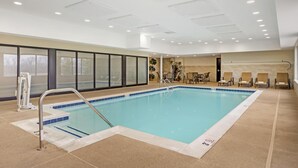 An indoor swimming pool with clear blue water, surrounded by beige tiled flooring and walls. There are lounge chairs and a small seating area with tables. - Best Western Plus Centralia Hotel & Suites (Centralia)