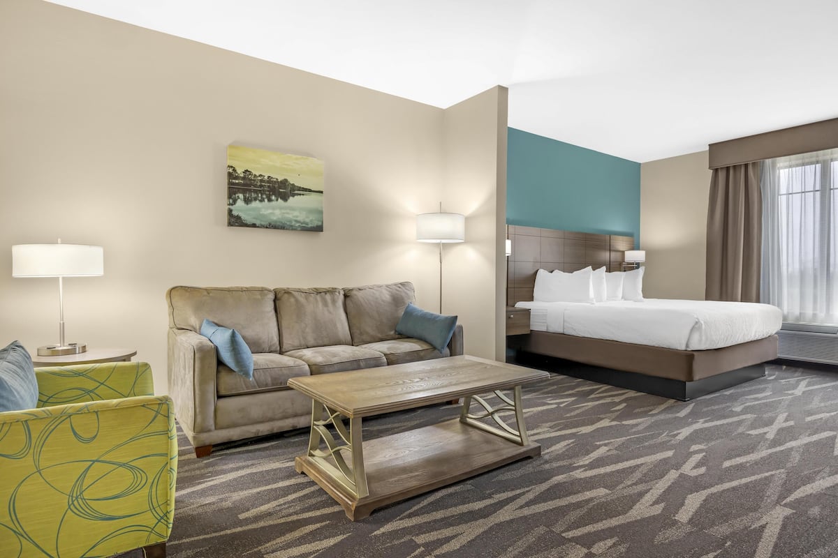 A hotel room with a bed, a sofa, a coffee table, and a painting on the wall.