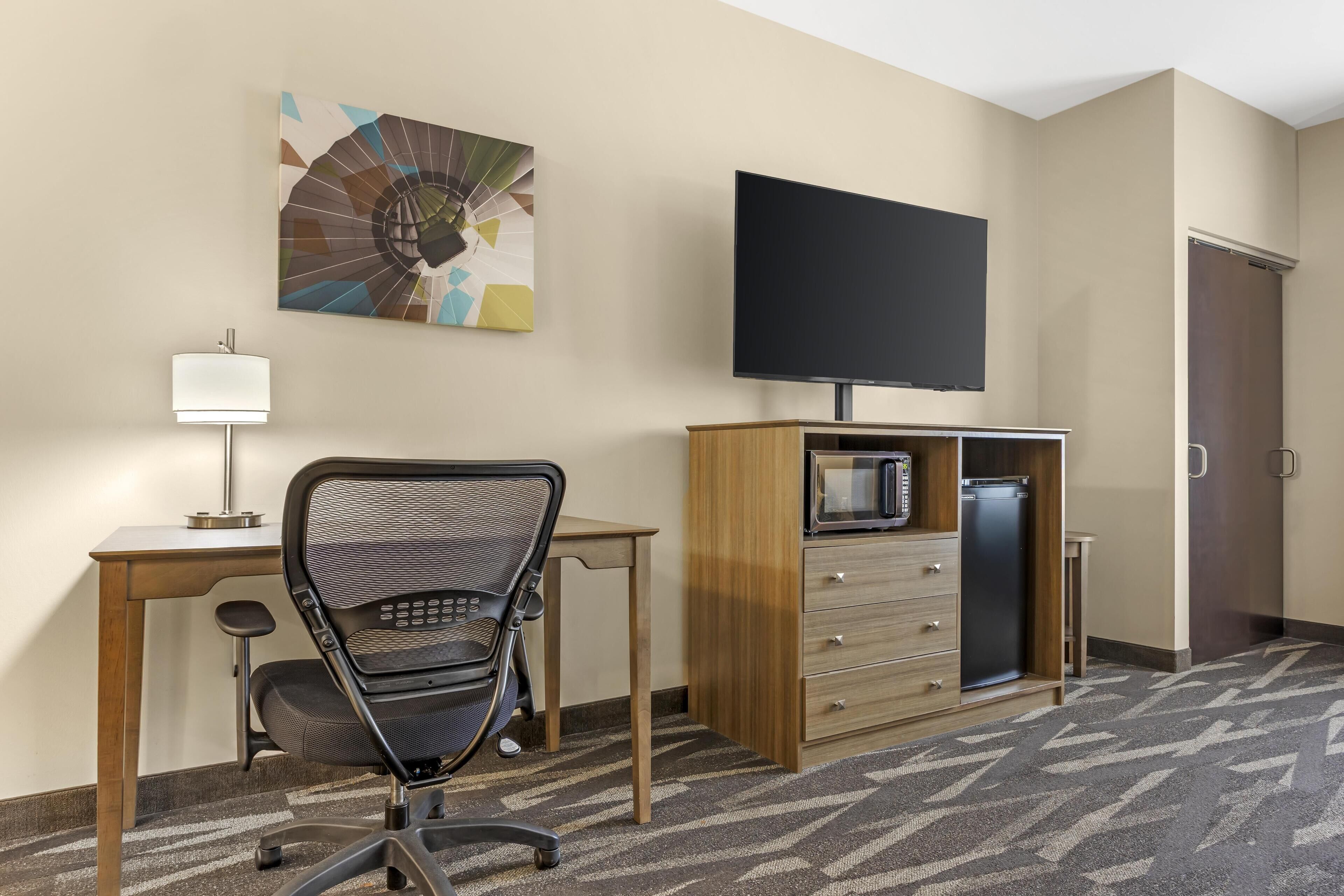 Habitación de hotel con escritorio, silla de oficina, televisor de pantalla plana, microondas y un armario.