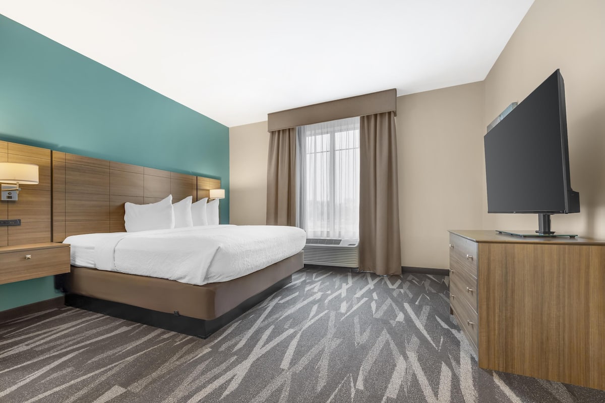 A hotel room with a bed, bedside table, lamp, TV, and a desk with drawers.