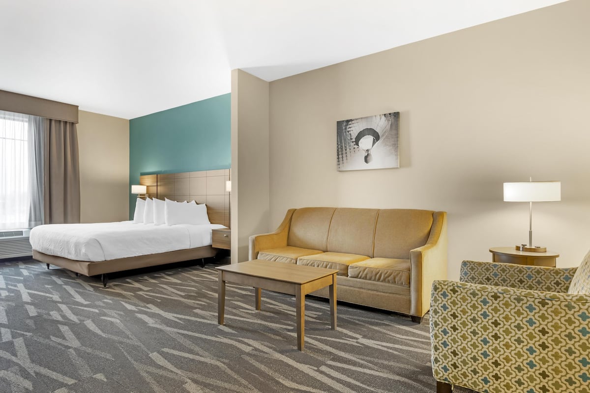 A hotel room with a bed, a sofa, a coffee table, and a small table with a lamp.