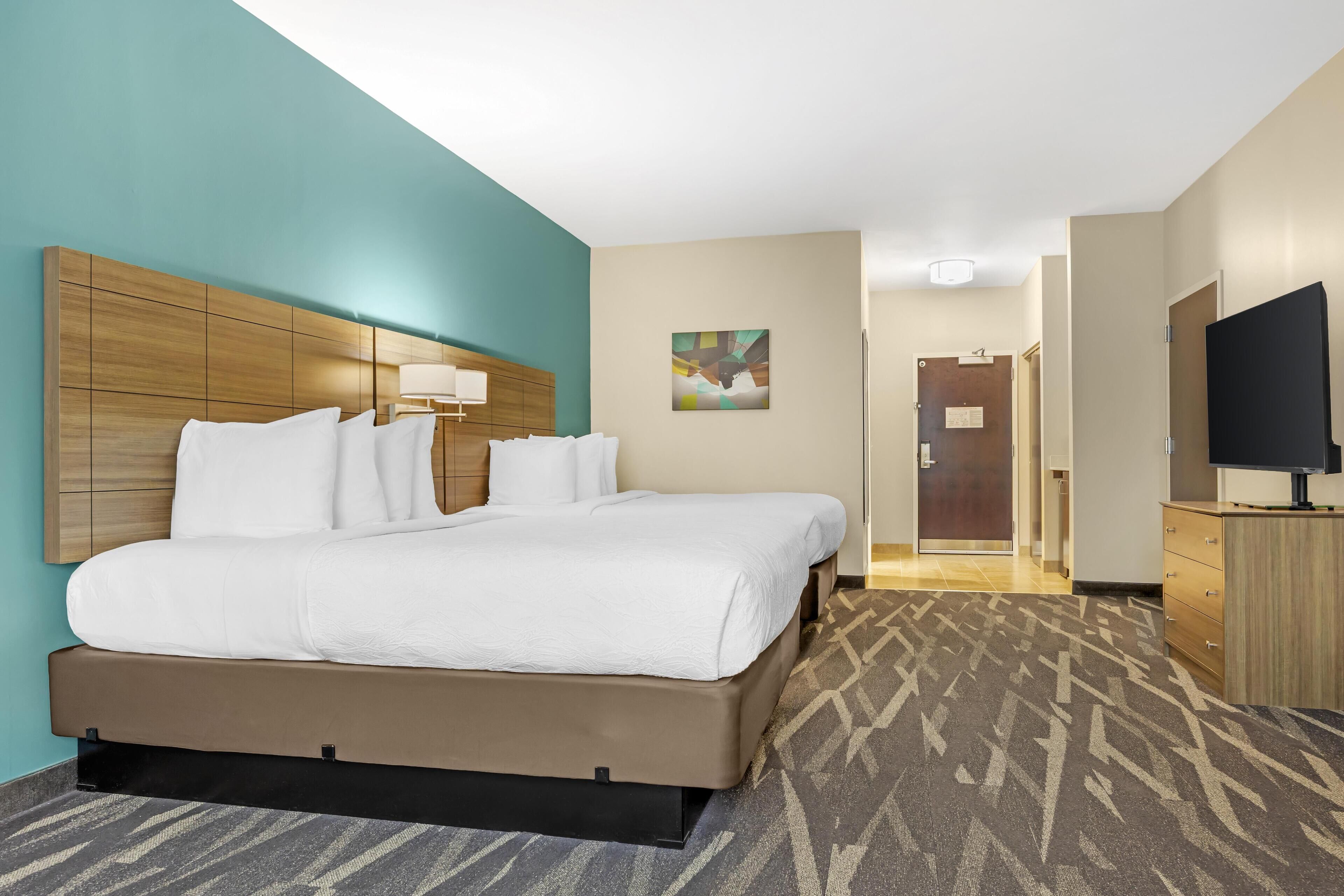 A hotel room with a large bed, a television, a desk, and a door leading to another room.