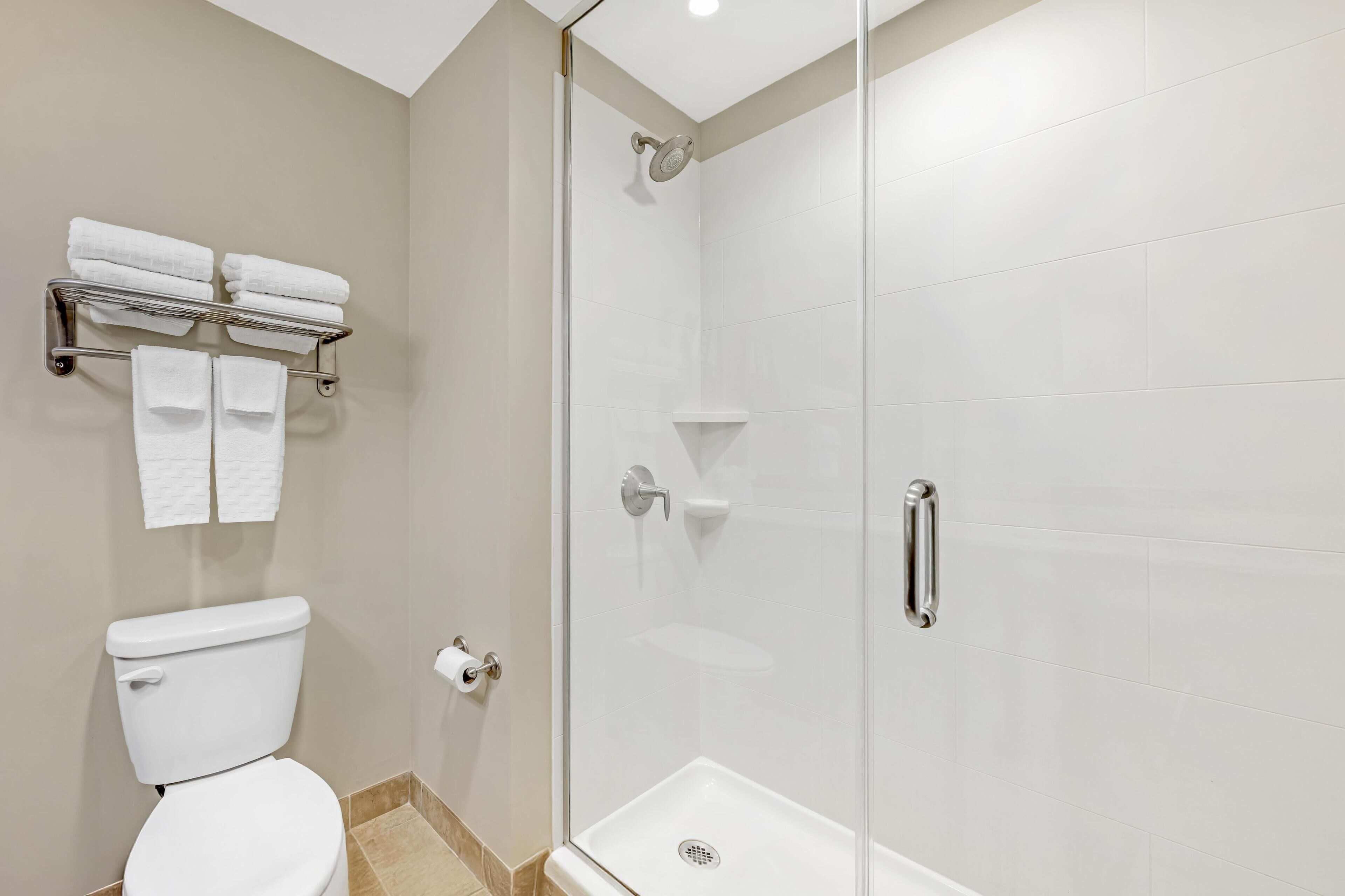 Une salle de bain moderne équipée de toilettes, d’une douche à parois de verre et d’un porte-serviettes avec des serviettes pliées.