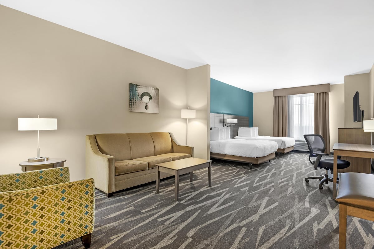 A hotel room with a sofa, two beds, a desk, and a patterned carpet.