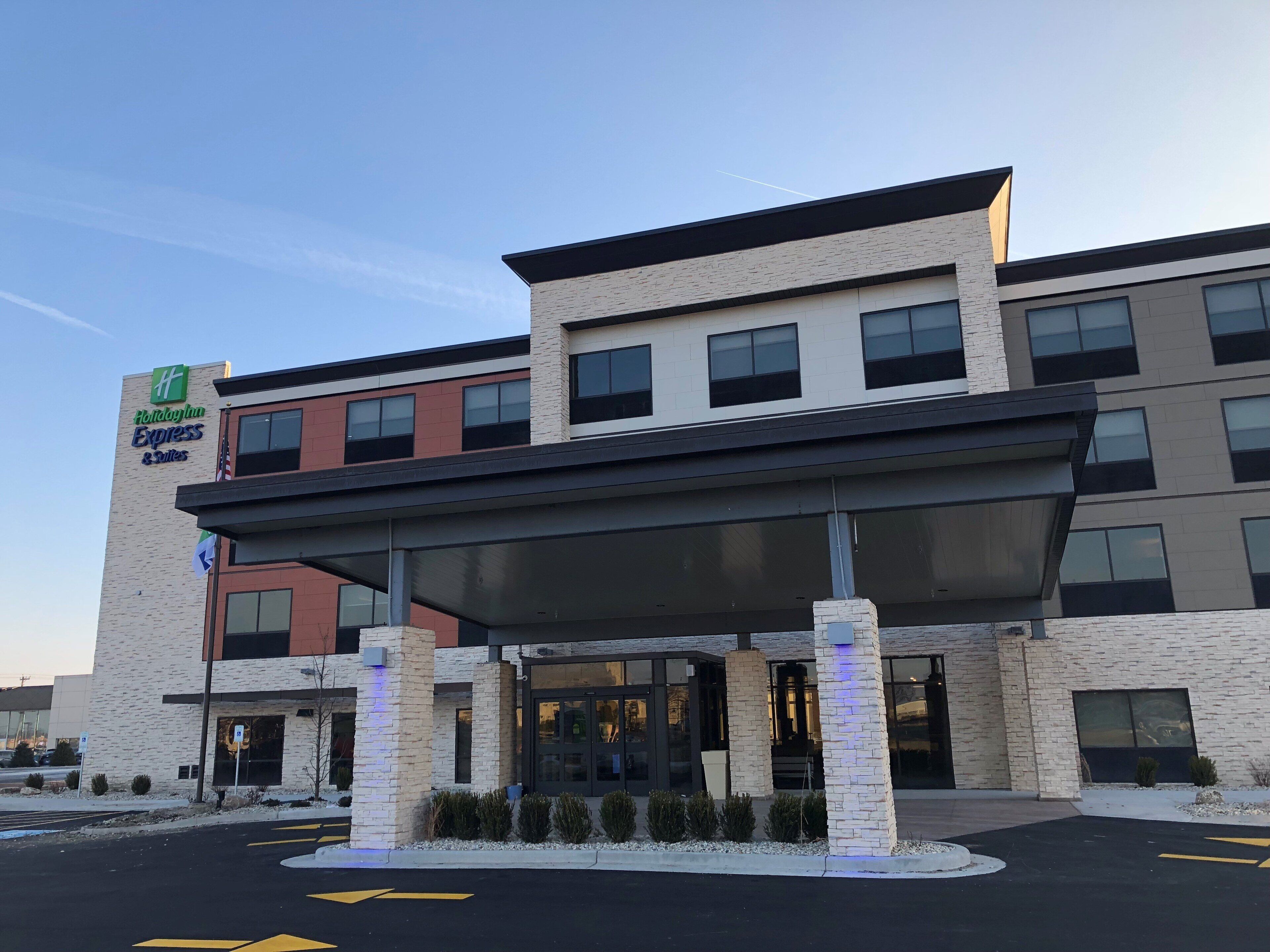 Un bâtiment de la chaîne Holiday Inn Express & Suites, doté d’un design moderne, avec une façade en briques, de grandes fenêtres et une entrée abritée.