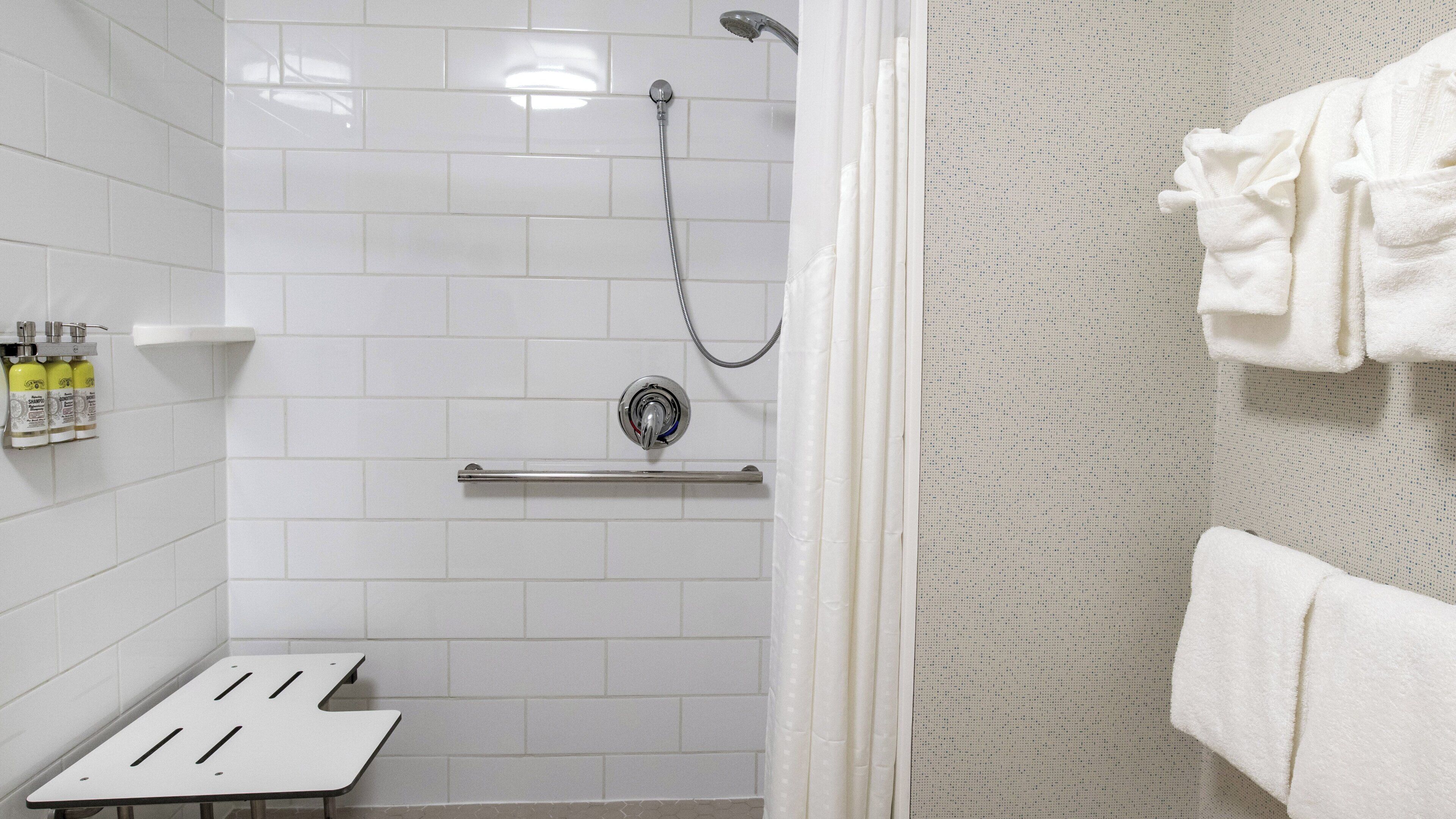 A shower with a handheld showerhead, a towel rack, and a shelf with toiletries.