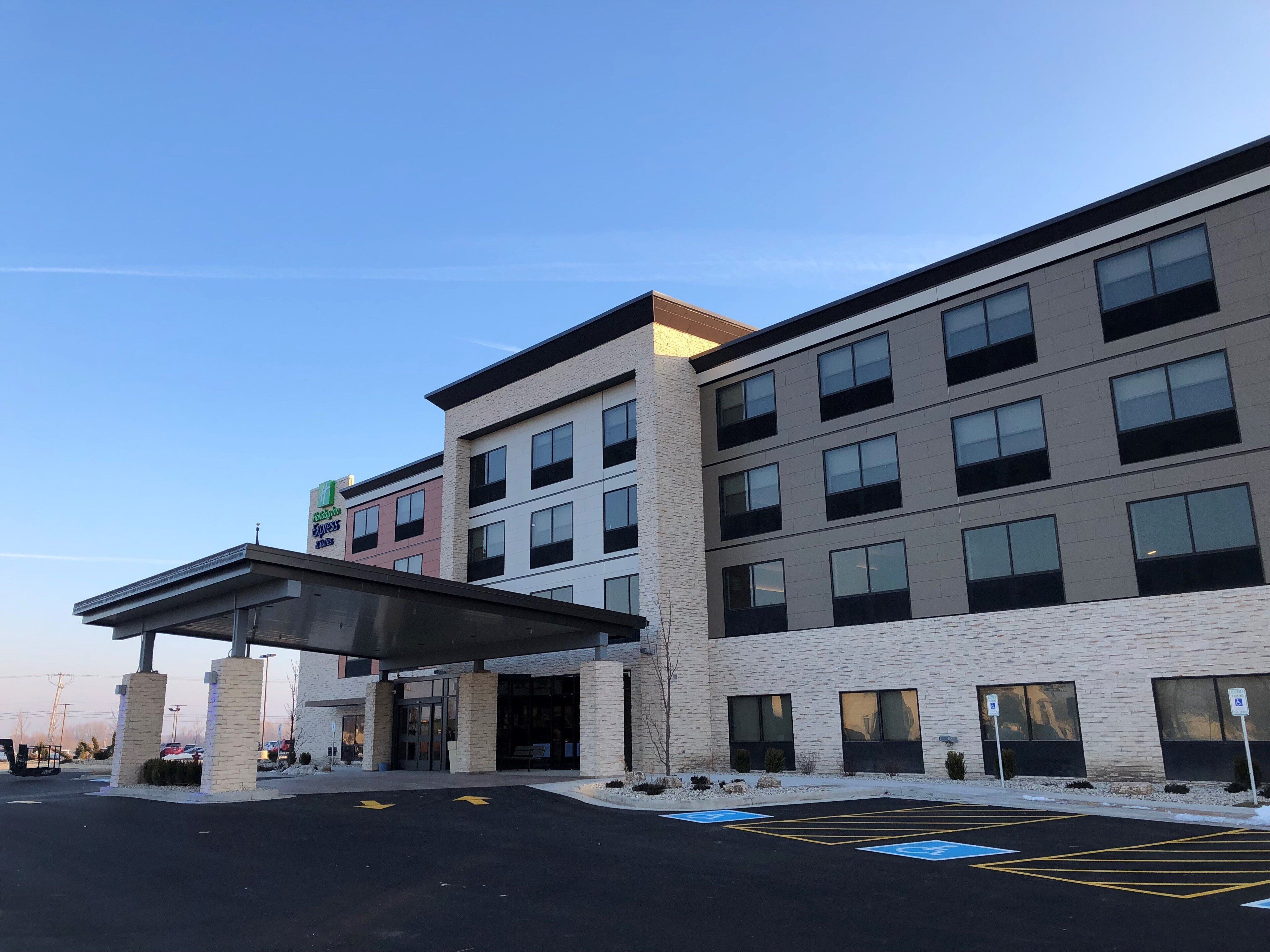 Un edificio de varios pisos con un diseño arquitectónico moderno, que cuenta con un acceso cubierto y un estacionamiento con espacios reservados para personas con movilidad reducida.