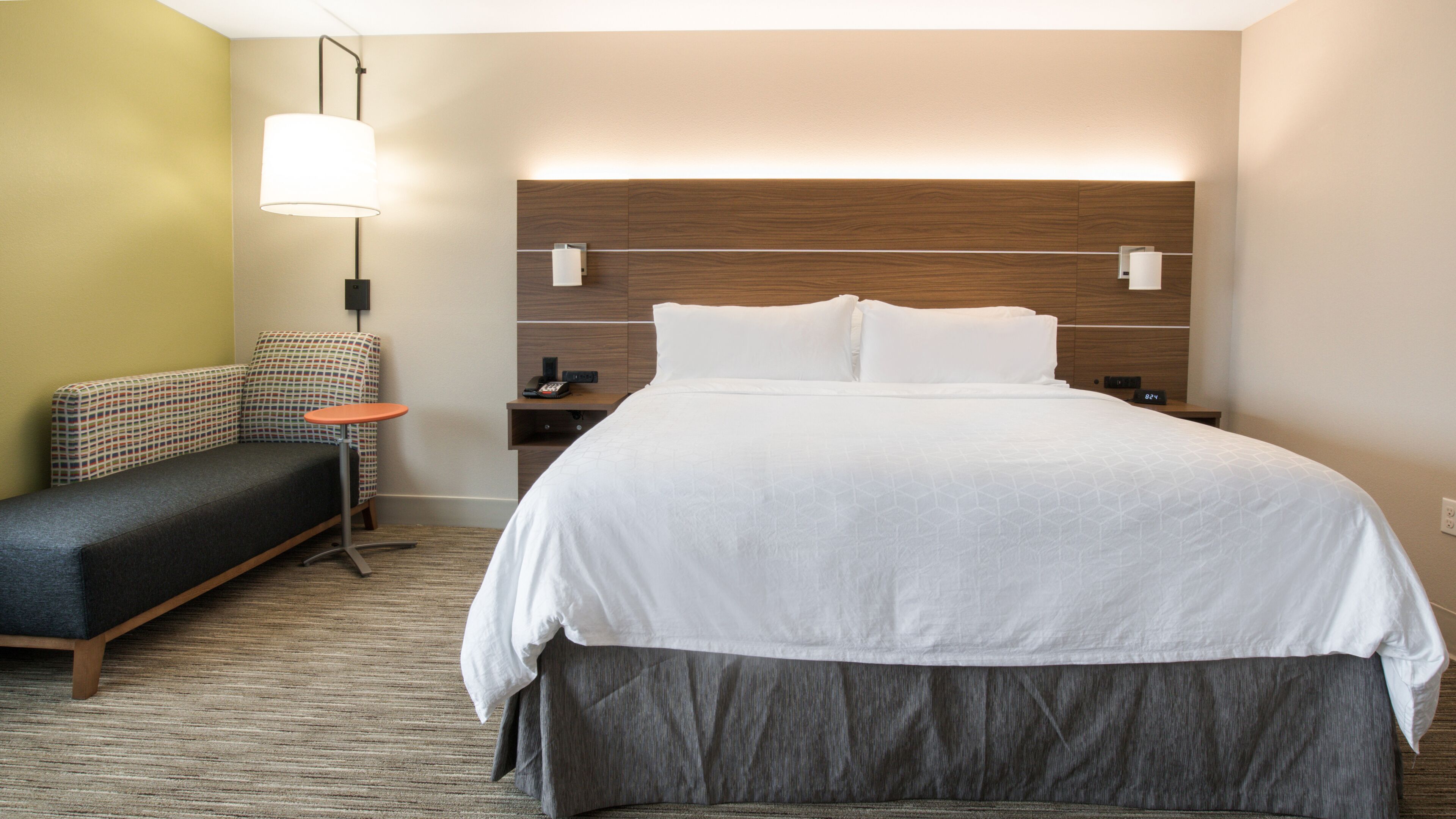 A hotel room with a large bed, a sofa, a small table, and a wall-mounted lamp.