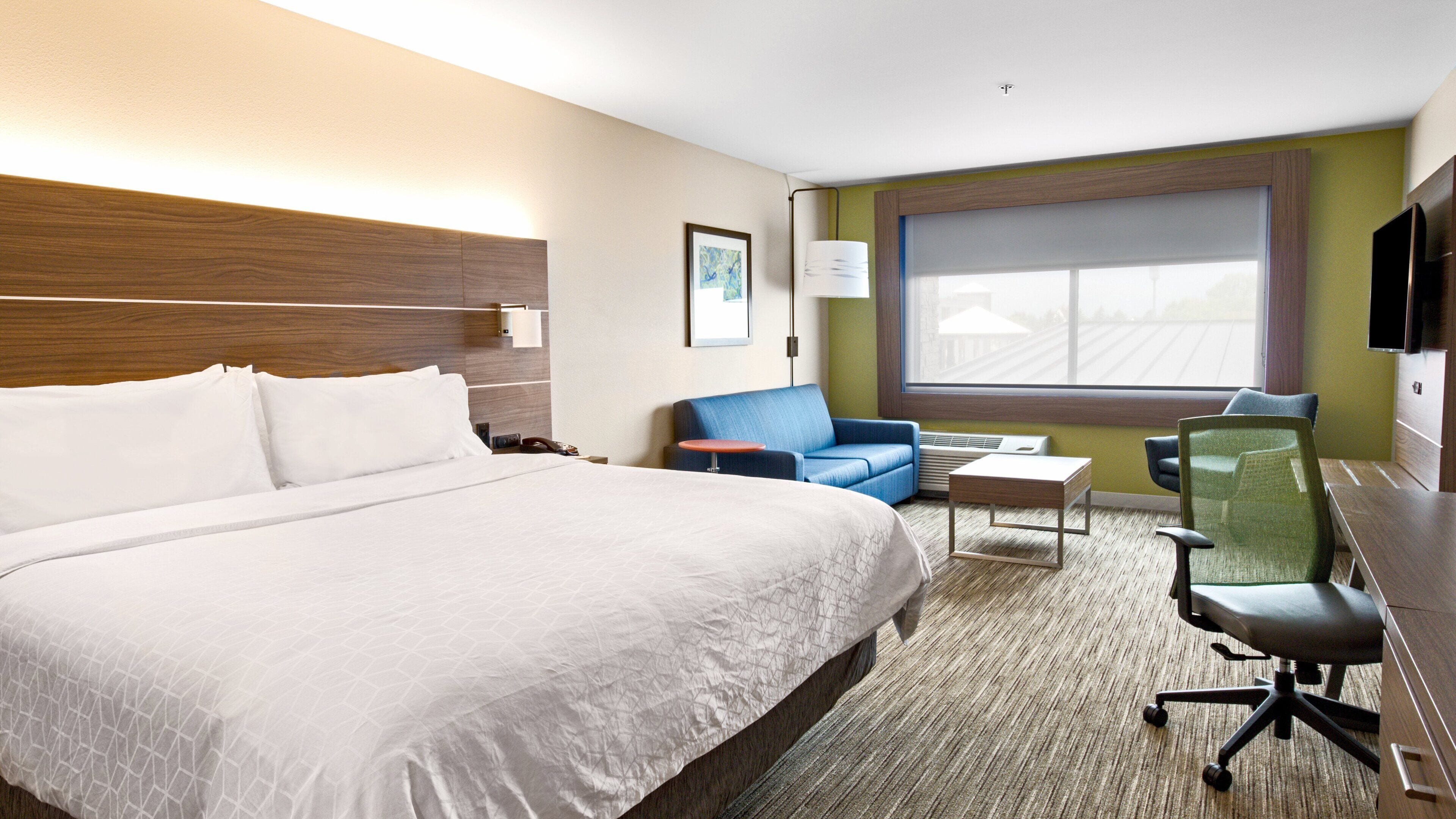 A hotel room with a large bed, a desk, a chair, a sofa, and a window with a view.