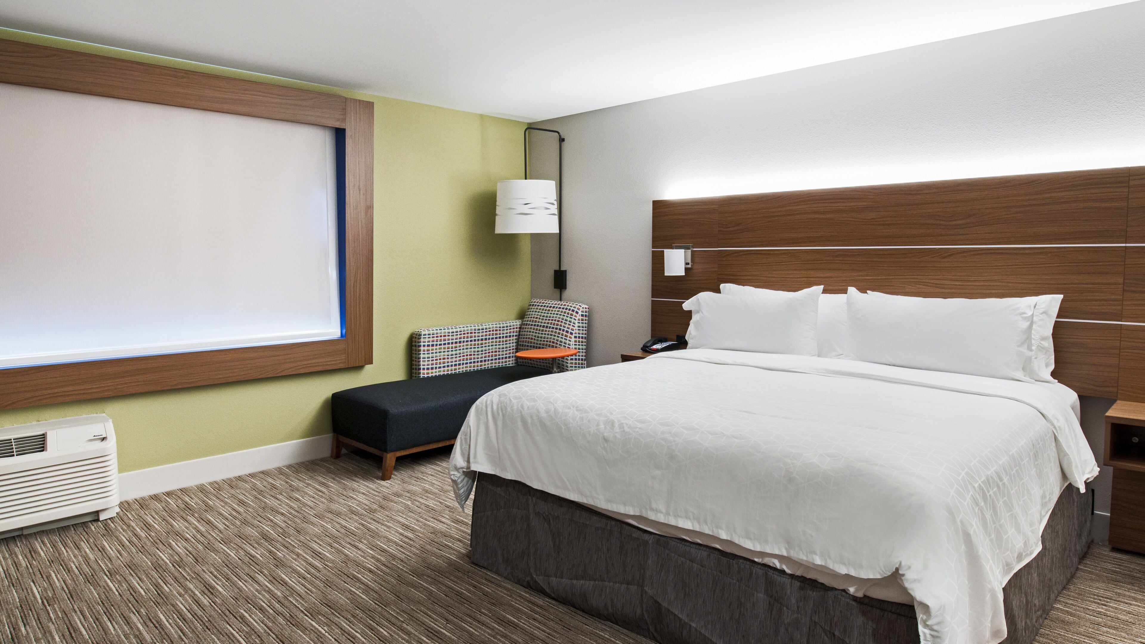 A hotel room with a large bed, a chair, a small table, and a window.
