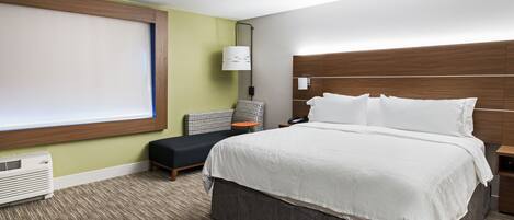A hotel room with a large bed, a chair, a small table, and a window.