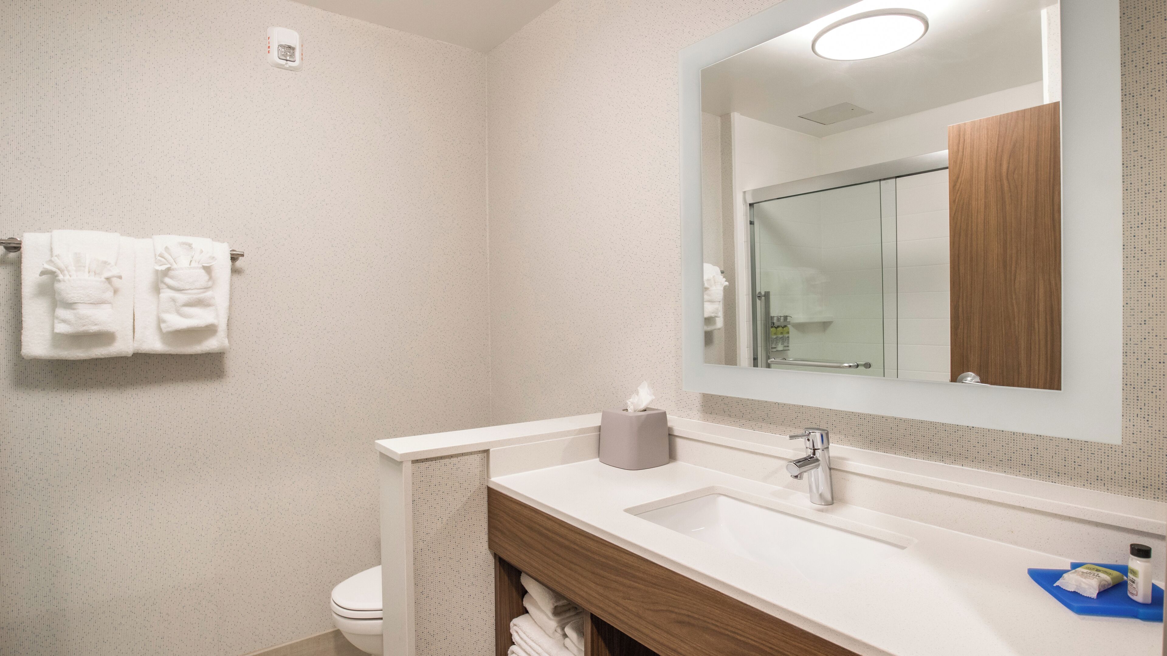 A bathroom with a toilet, sink, mirror, and towel rack.