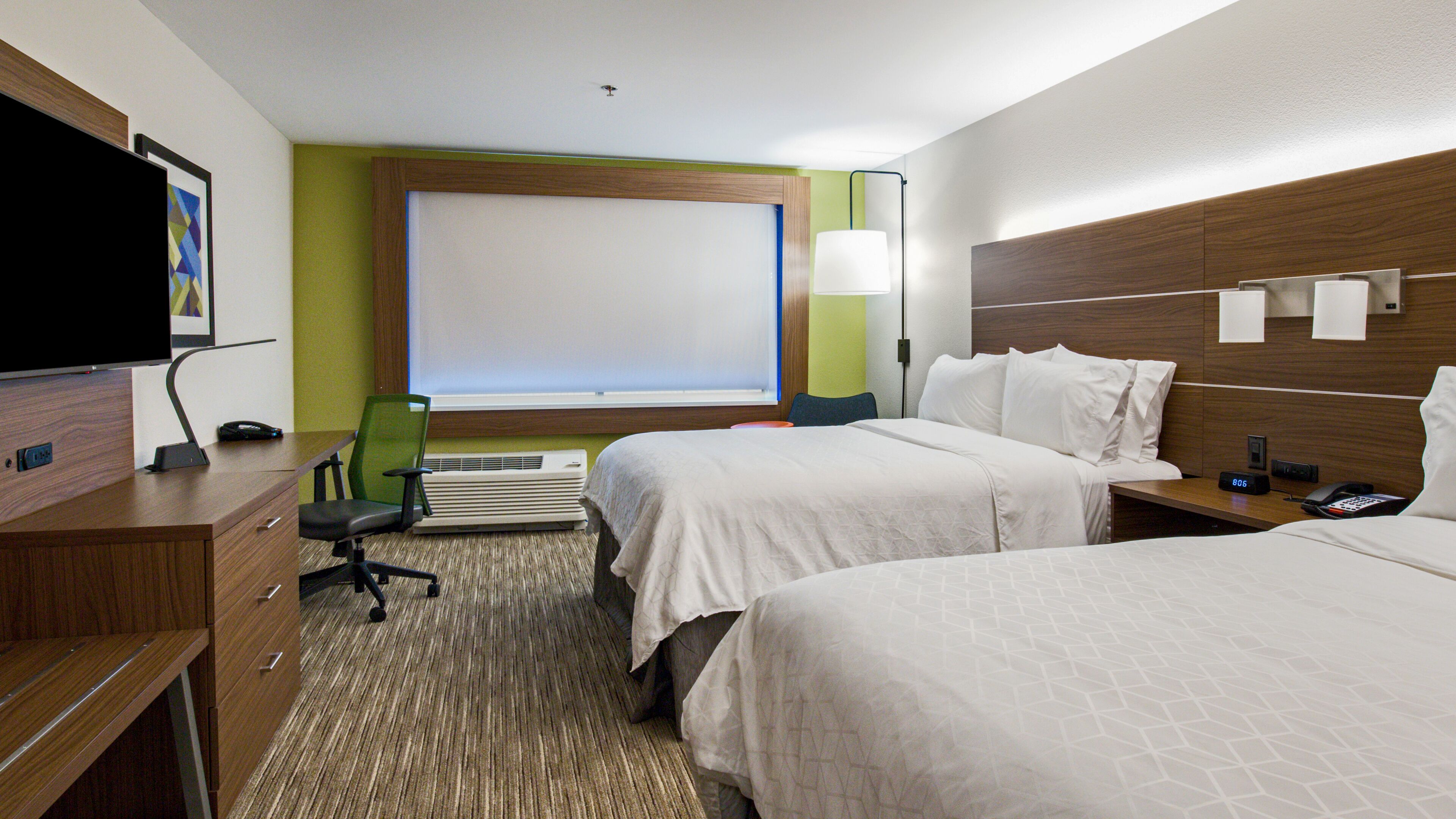Habitación de hotel con dos camas, un escritorio con silla, televisor y ventana con persianas.