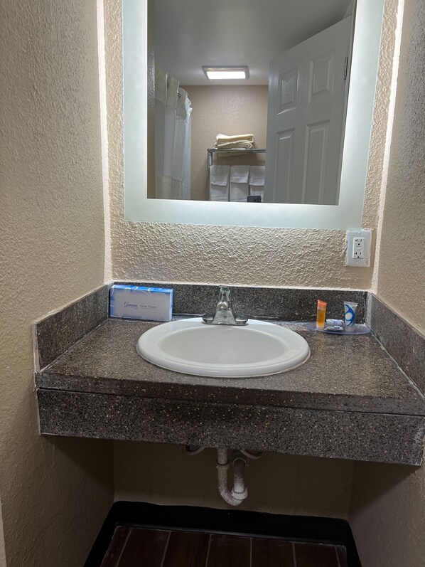 Un baño con lavamanos de encimera de granito, un espejo encima y un perchero con toallas.