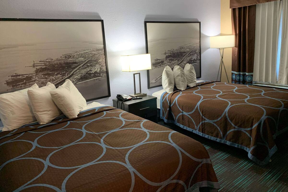 Habitación de hotel con dos camas, una mesita de noche, una lámpara y un cuadro grande en la pared.