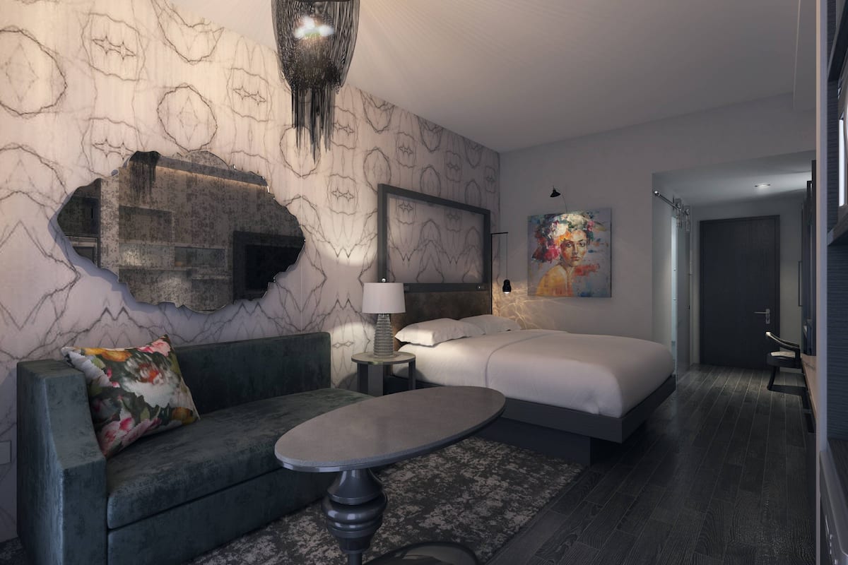 A modern hotel room with a marble-patterned wall, a large bed, a sofa, a small round table, and a painting on the wall.