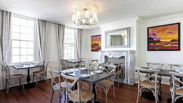 A dining room with a fireplace, wooden flooring, and a chandelier.