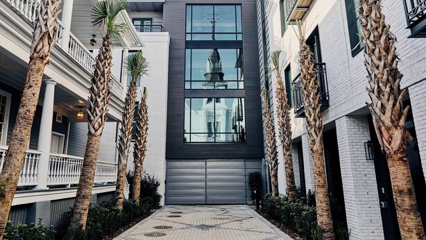 A modern building with a central glass facade, flanked by palm trees and white brick walls. - Hotel Bella Grace (Charleston)