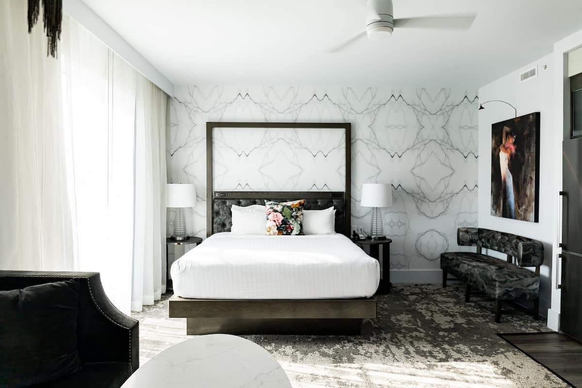 A modern hotel room with a large bed, two bedside tables, a bench, and a ceiling fan.