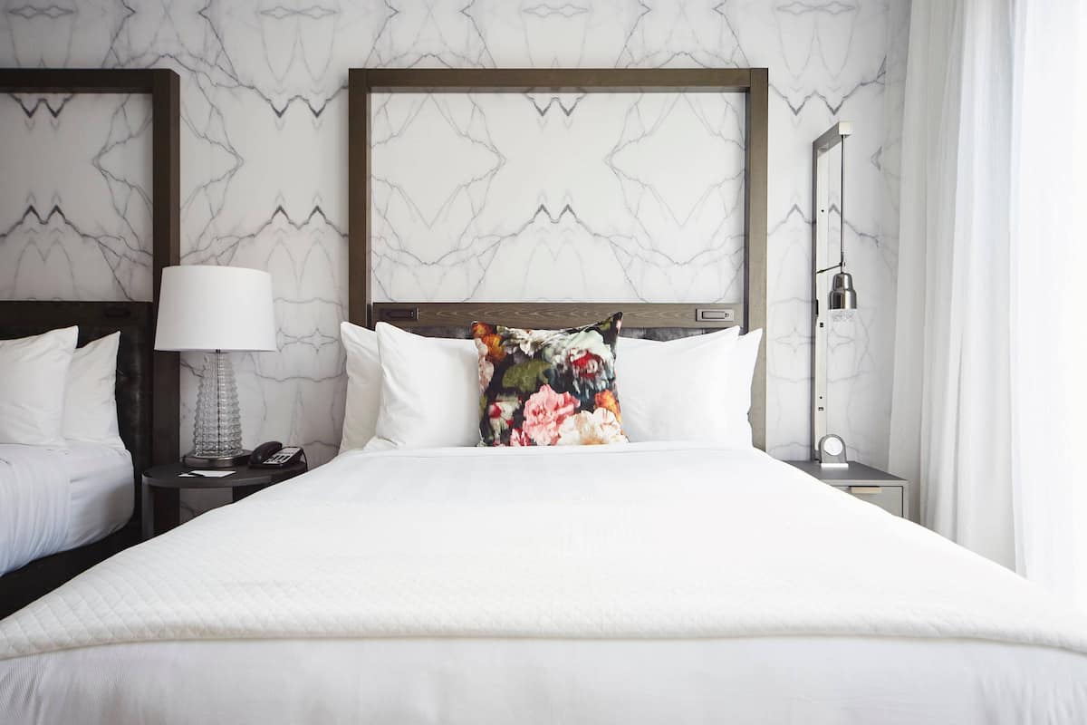 A hotel room with a large bed, two bedside tables, a nightstand, a lamp, a phone, and a wall-mounted light fixture.