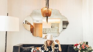 A living room with a dark sofa, a white lamp, a large mirror, and a small table with a vase of flowers. - Hotel Bella Grace (Charleston)