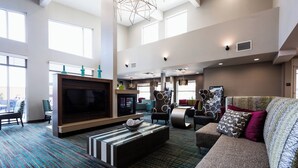 A spacious living room with a large flat-screen TV, comfortable seating, a patterned carpet, and large windows providing natural light. - Residence Inn by Marriott Oklahoma City Airport (Oklahoma City)