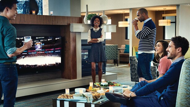 A group of people in a modern hotel lobby with a flat-screen TV, a buffet table, and comfortable seating areas. - Residence Inn by Marriott Oklahoma City Airport (Oklahoma City)