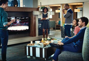 A group of people in a modern hotel lobby with a flat-screen TV, a buffet table, and comfortable seating areas. - Residence Inn by Marriott Oklahoma City Airport (Oklahoma City)