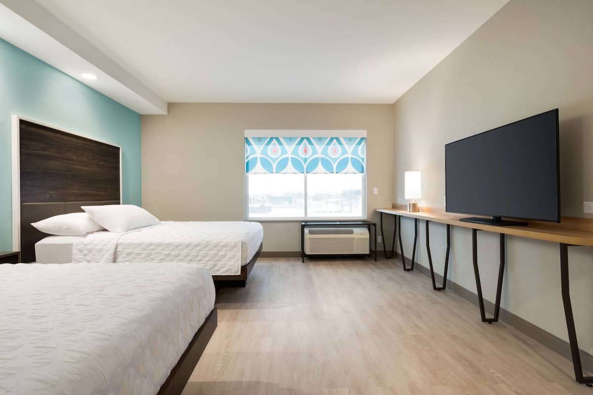 Ein Hotelzimmer mit zwei Betten, einem Fernseher, einem Schreibtisch und einem Fenster mit dekorativem Muster.