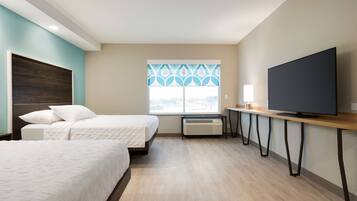 A hotel room with two beds, a TV, a desk, and a window with a decorative pattern.