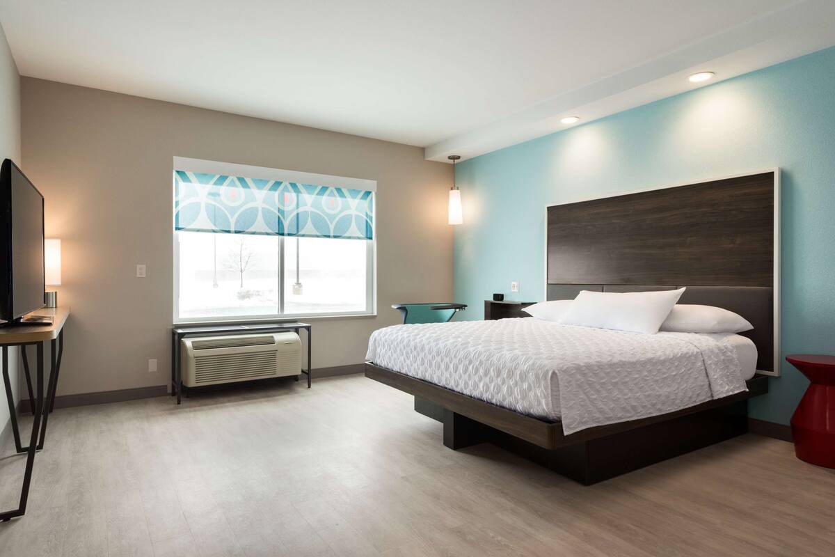 Ein modernes Hotelzimmer mit Bett, Schreibtisch, Stuhl und Fernseher.