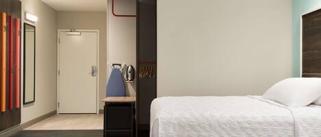 A hotel room with a bed, a desk, and a door.