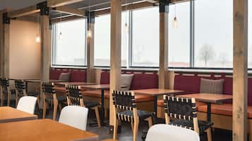 L’intérieur d’un restaurant avec des tables et des chaises en bois, de grandes fenêtres et des lampes suspendues.
