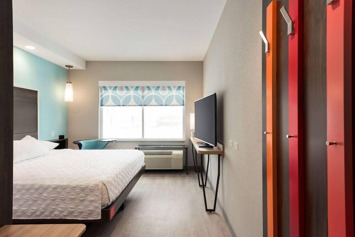 Ein Hotelzimmer mit einem Bett, einem Fernseher, einem Schreibtisch und einem Fenster mit gemusterten Vorhängen.