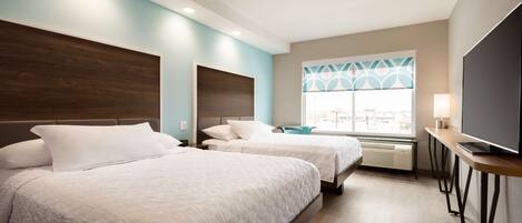 A hotel room with two beds, a TV, a desk, and a window with a view.