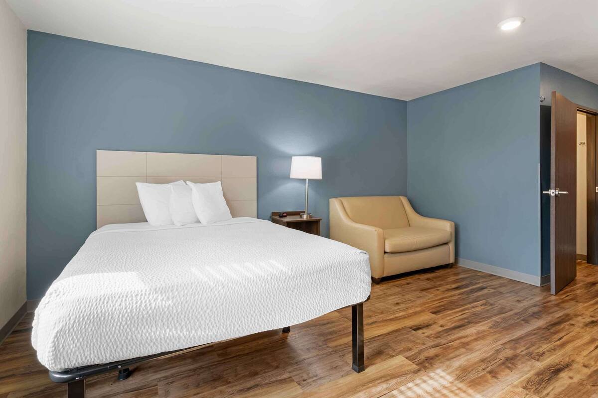 Una habitación de hotel con cama, una silla, una mesita de noche y una lámpara.