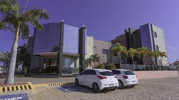 A modern building with a glass facade, parked cars, and palm trees.