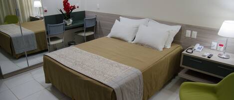 Una habitación de hotel con una cama grande, un escritorio, una silla y una mesita de noche con una lámpara.