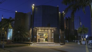A modern hotel entrance with a glass facade, a well-lit entrance, and a paved driveway. - Vitoria Palace Hotel (Mossoro)