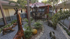 A courtyard with a giraffe statue, a dog statue, and a yellow spherical object surrounded by plants and a paved area. - Vitoria Palace Hotel (Mossoro)