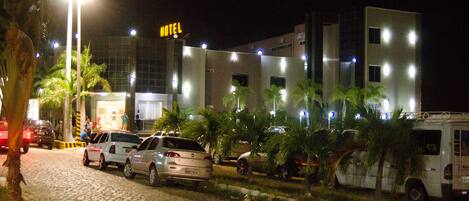 A hotel with a modern design, featuring a prominent 'HOTEL' sign, a paved driveway, and several parked cars.