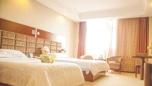 Ein Hotelzimmer mit zwei Betten, einem großen Teddybären auf einem Bett, einem Sessel, einem kleinen Tisch und einem Fenster mit Vorhängen.