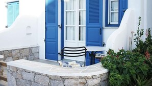A stone wall, a white table with a black chair, and a blue door with shutters. - Paraporti Hotel (Folegandros)