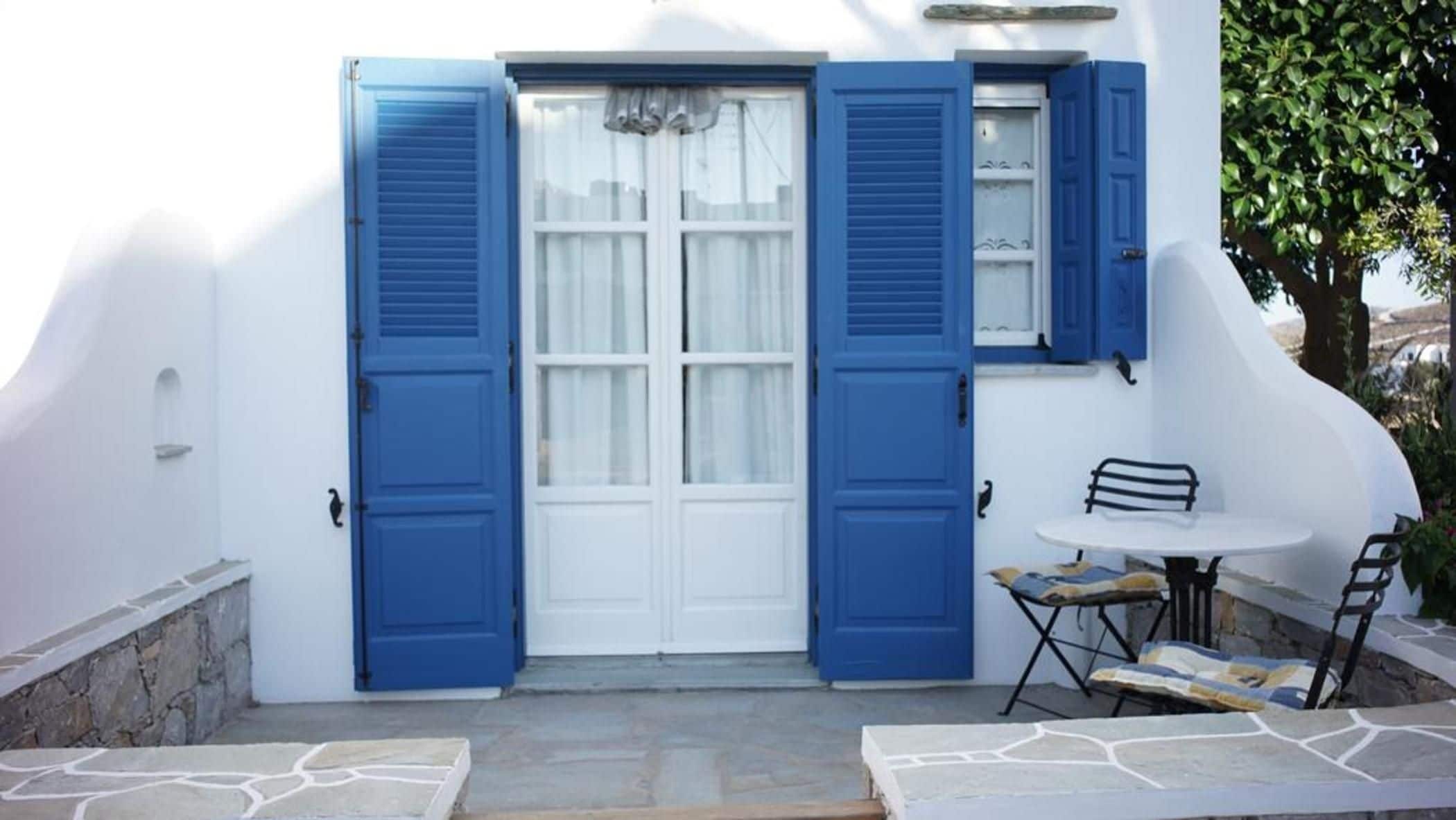 A white building with blue shutters, a white door, and a small outdoor seating area with a table and chairs.