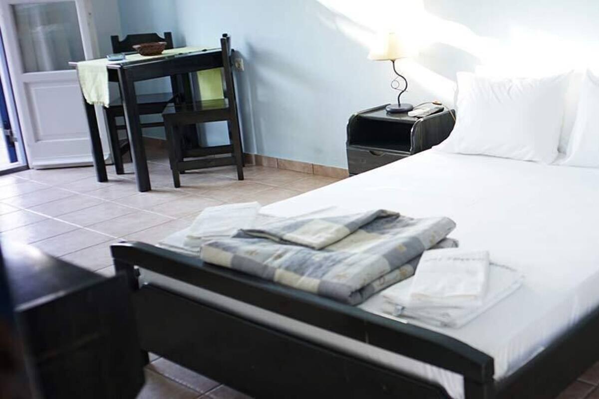 Una cama bien hecha con almohadas, una mesita de noche con lámpara, una silla y una pequeña mesa con un cuenco.