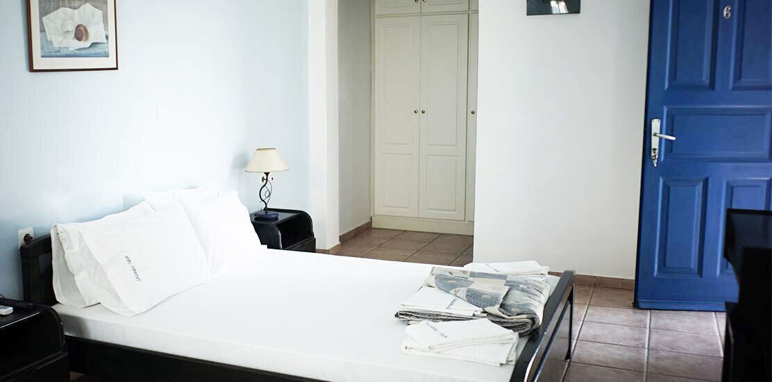 Ein Schlafzimmer mit Bett, Nachttisch, Lampe, Kleiderschrank und einer blauen Tür.