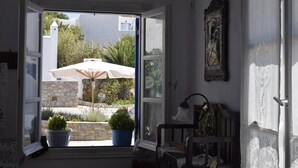 An open door leading to a balcony with a white umbrella, potted plants, and a stone wall. - Paraporti Hotel (Folegandros)